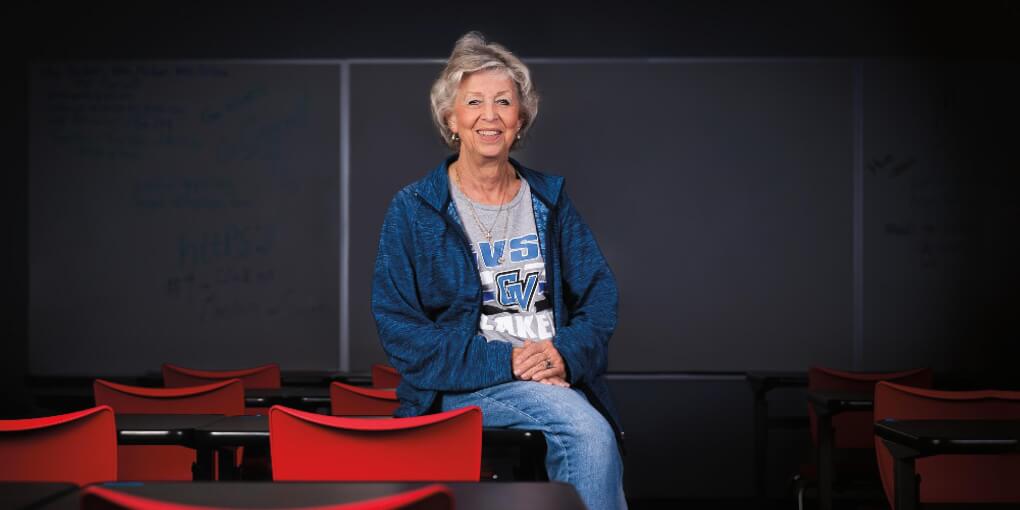 Pat Baker sits in her classroom wearing a Grand Valley shirt